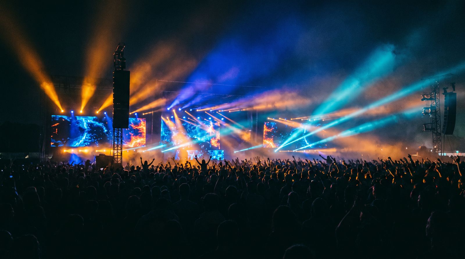 Festival al aire libre de noche: una multitud con las manos arriba frente a un gran escenario con pantallas LED.